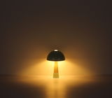 Moderne Tischleuchte mit rundem, dunklem Schirm und konischem Sockel, frontal beleuchtet in dunkler Umgebung.