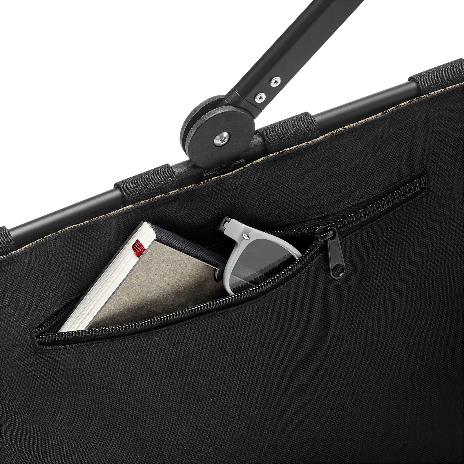 Nahaufnahme einer schwarzen Tasche mit Reißverschluss, die ein Notizbuch und eine Sonnenbrille enthält, mit Fokus auf den oberen Rand und den Griff.