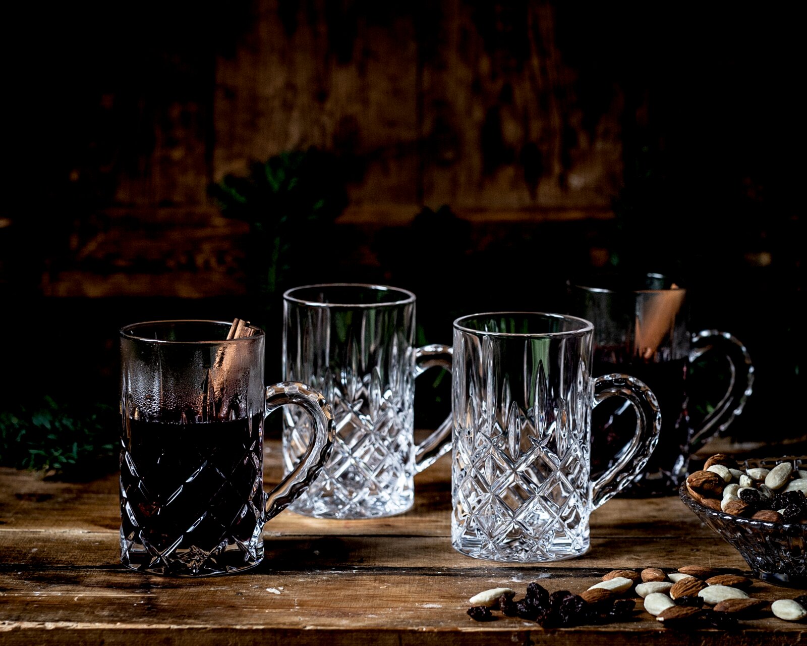 Kristallen mokken met klassiek geslepen patroon, vanuit schuin vooraanzicht op een rustieke houten tafel, deels gevuld met een donkere warme drank.