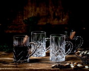 Kristallen mokken met klassiek geslepen patroon, vanuit schuin vooraanzicht op een rustieke houten tafel, deels gevuld met een donkere warme drank.