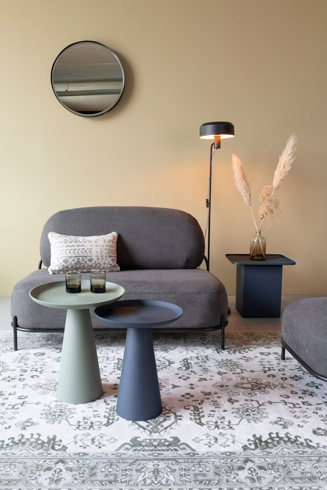 Z2 Beistelltisch RINGAR Zwei moderne Beistelltische in verschiedenen Farben, im Vordergrund einer stilvollen Wohnzimmerumgebung mit Sofa, Stehlampe und dekorativem Teppich, aus seitlicher Perspektive.