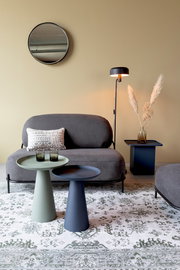 Zwei moderne Beistelltische in verschiedenen Farben, im Vordergrund einer stilvollen Wohnzimmerumgebung mit Sofa, Stehlampe und dekorativem Teppich, aus seitlicher Perspektive.