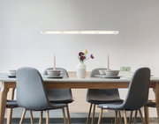 Moderne LED-Hängeleuchte über einem Esstisch mit vier grauen Stühlen, aus seitlicher Perspektive fotografiert.