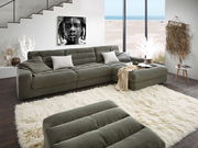 Grüne Longchairkombination in modernem Wohnzimmer mit Blick auf das Meer durch große Fenster, dekoriert mit Kissen und Decke, fotografiert aus einer leicht erhöhten Perspektive.