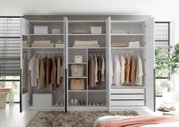 Großer weißer Kleiderschrank mit vier geöffneten Drehtüren, Kleiderstangen, Regalfächern und drei Schubladen, frontal in einem hellen Schlafzimmer gezeigt