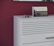 Nahaufnahme einer weißen Garderobenkombination mit Schubladen und einem Schlüsselbund sowie einem Briefhalter auf der Oberfläche, vor einer weinroten Wand.