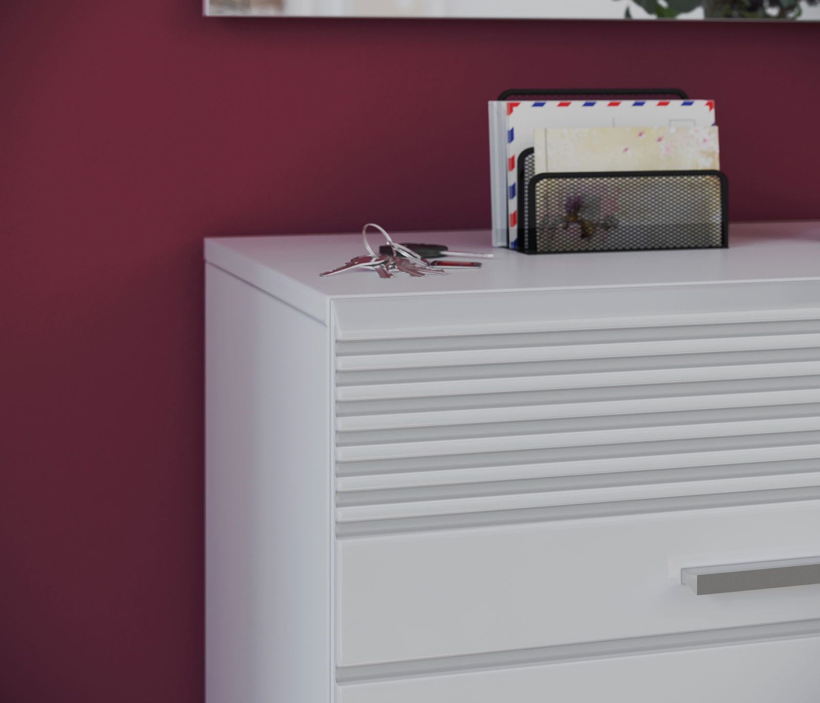 Nahaufnahme einer weißen Garderobenkombination mit Schubladen und einem Schlüsselbund sowie einem Briefhalter auf der Oberfläche, vor einer weinroten Wand.