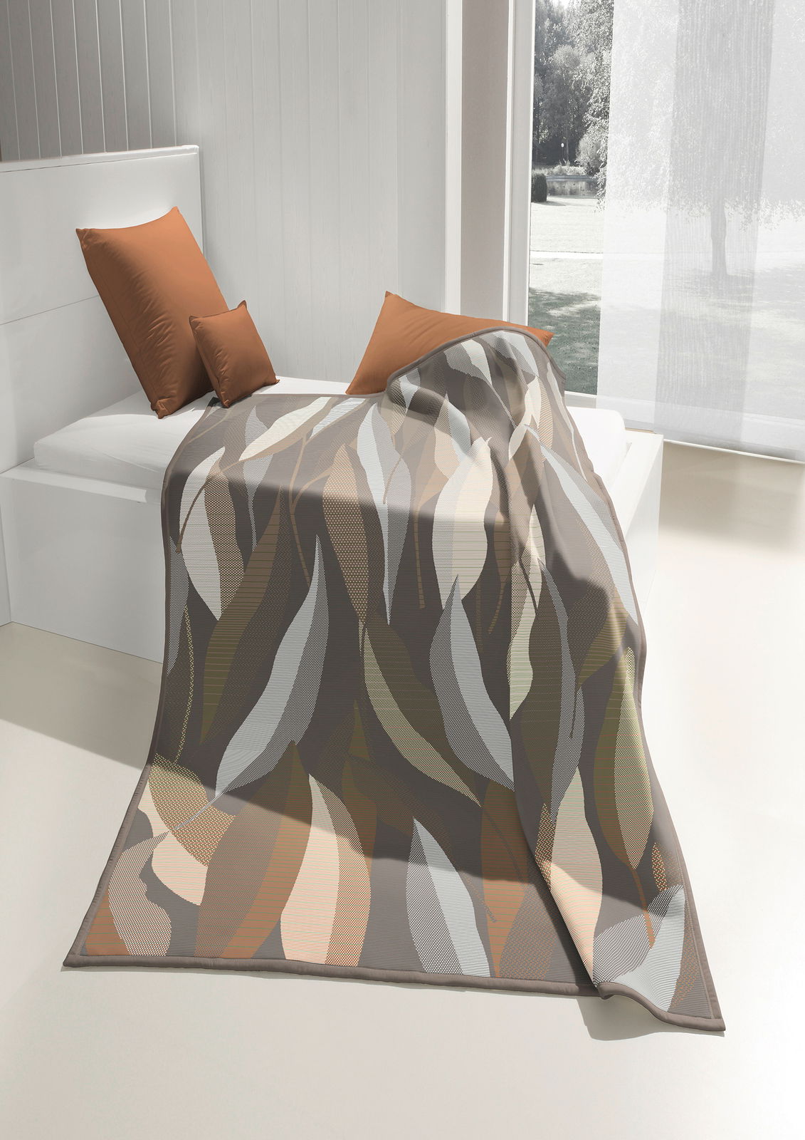 biederlack Wohndecke COTTON HOME Wohndecke mit abstraktem Blattmuster in Erdtönen, drapiert auf einem Bett in einem hellen Raum mit Blick nach draußen.