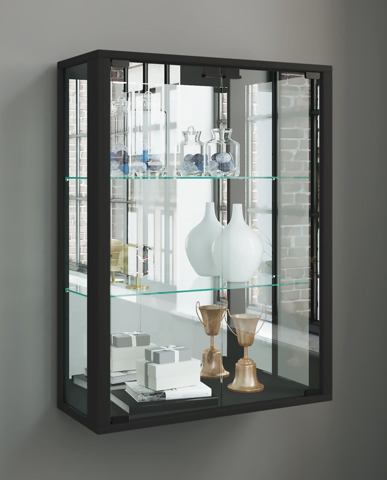 Schwarze Glasvitrine mit Glastüren und zwei Glasböden, bestückt mit Dekogläsern, weißen Vasen, Büchern und goldfarbenen Pokalen, fotografiert in leichter Frontansicht mit Perspektive von links.