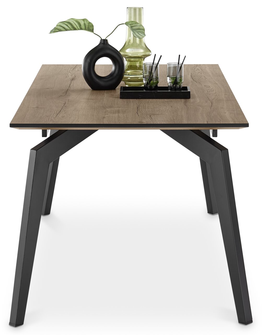 Moderner Esstisch 160x90 cm mit Holzoptik und schwarzen Metallbeinen, frontal fotografiert. Dekoriert mit einer Vase, einem Glasgefäß und zwei Gläsern.