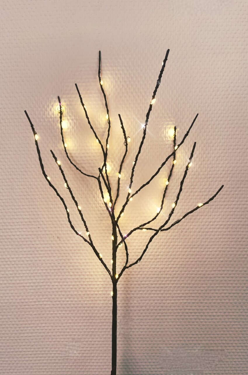 LED-Zweig mit warmweißen Lichtern, frontal fotografiert vor einer strukturierten Wand.