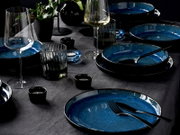 Elegantes Tafelservice 12-tlg in Blau und Schwarz, präsentiert auf einem gedeckten Tisch mit Gläsern und Dekoration, aus seitlicher Perspektive.