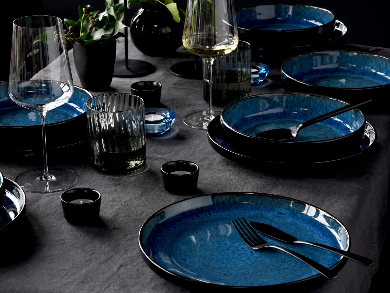 Elegantes Tafelservice 12-tlg in Blau und Schwarz, präsentiert auf einem gedeckten Tisch mit Gläsern und Dekoration, aus seitlicher Perspektive.
