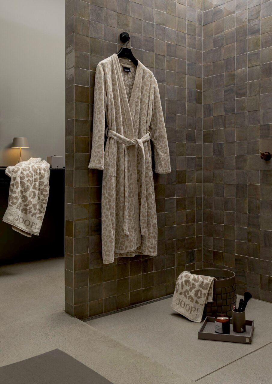 Beiger Bademantel mit Leopardenmuster, aufgehängt an einer Wand in einem stilvollen Badezimmer. Perspektive: Frontalansicht.
