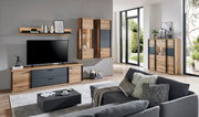 Modernes Wohnzimmer mit TV-Lowboard, Wandregal, Hänge-Vitrine und Sideboard in Holzoptik mit anthrazitfarbenen Fronten; Aufnahme aus schräger Frontperspektive im hellen Raum mit großen Fenstern.