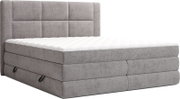 Grijs gestoffeerd boxspringbed met gewatteerd hoofdbord en witte topmatras, schuin van voren gefotografeerd (driekwartaanzicht).