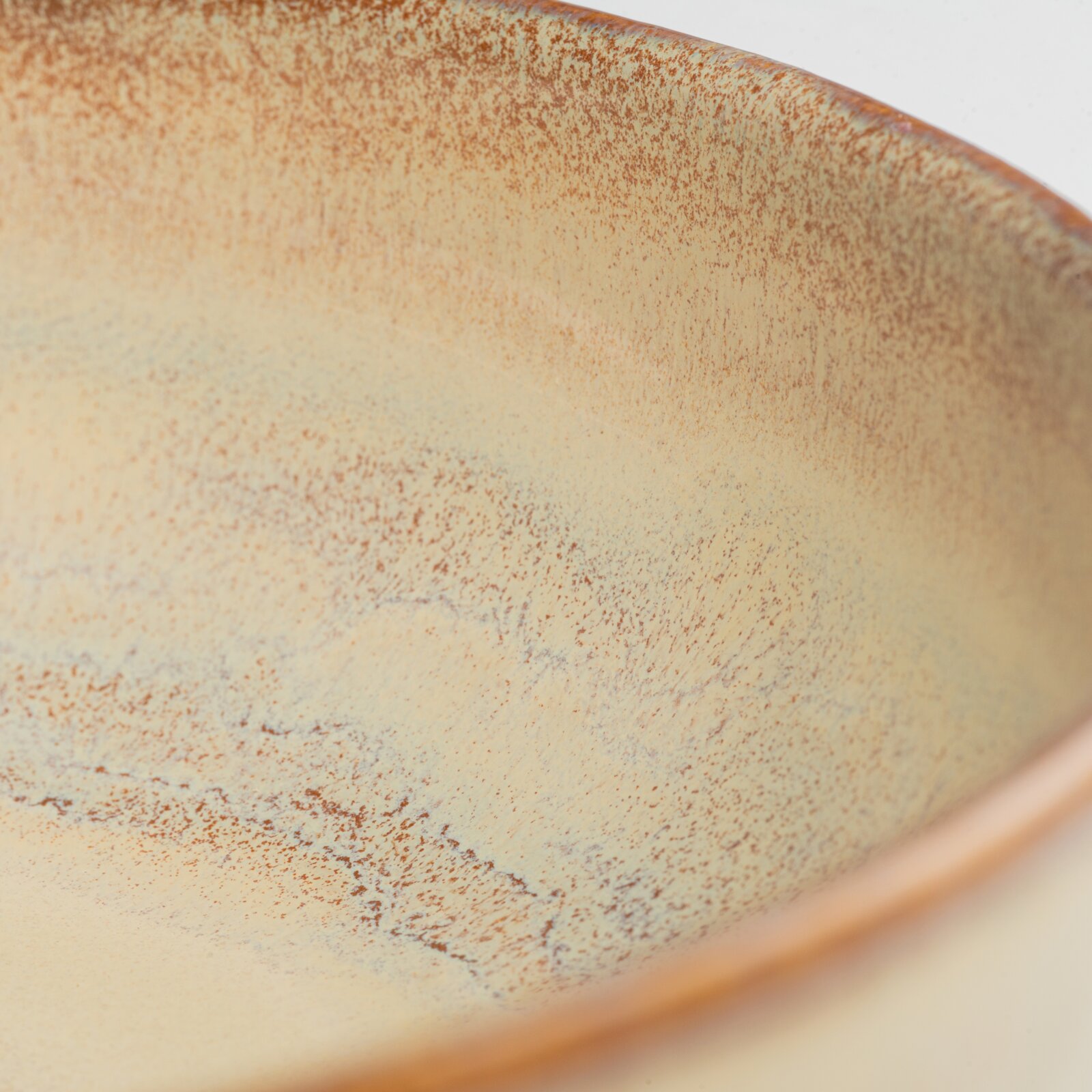 Detailaufnahme einer glasierten Keramikschale in Beige mit braunen Sprenkeln und leicht irisierendem Rand, schräg von oben fotografiert.