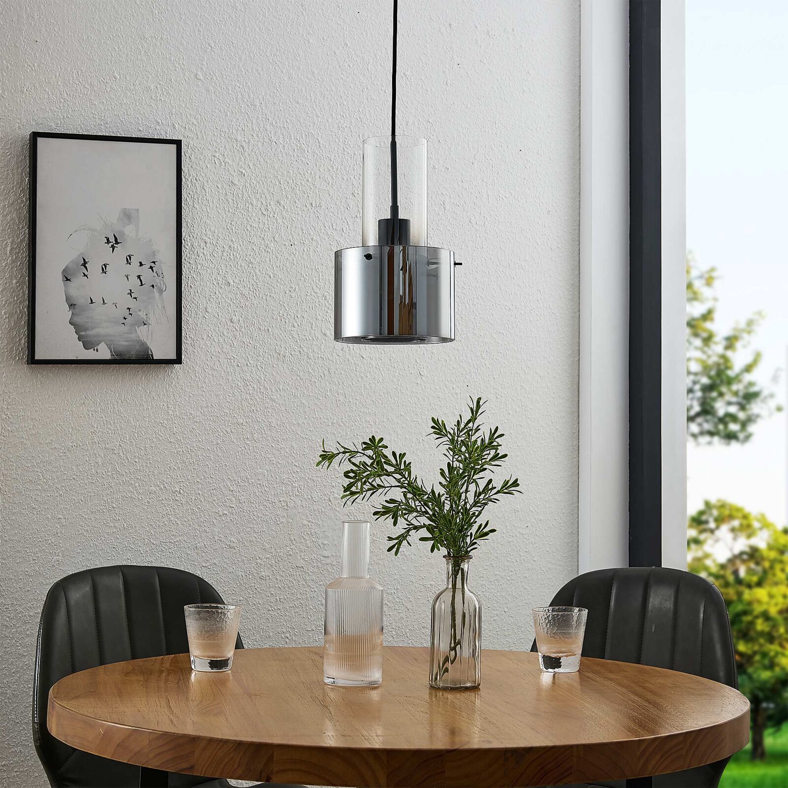 Moderne Hängeleuchte in einem Esszimmer, mit einem runden Holztisch und zwei schwarzen Stühlen, aus der Perspektive von vorne betrachtet.