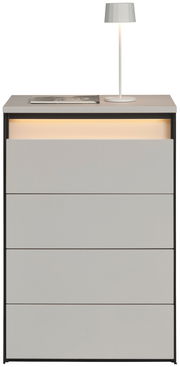 Hochkommode mit vier Schubladen, grauer Oberfläche und integrierter Beleuchtung, frontal betrachtet. Auf der Oberseite steht eine weiße Lampe und ein Buch.