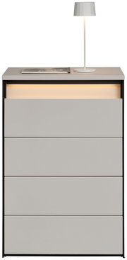 Hochkommode mit vier Schubladen, grauer Oberfläche und integrierter Beleuchtung, frontal betrachtet. Auf der Oberseite steht eine weiße Lampe und ein Buch.