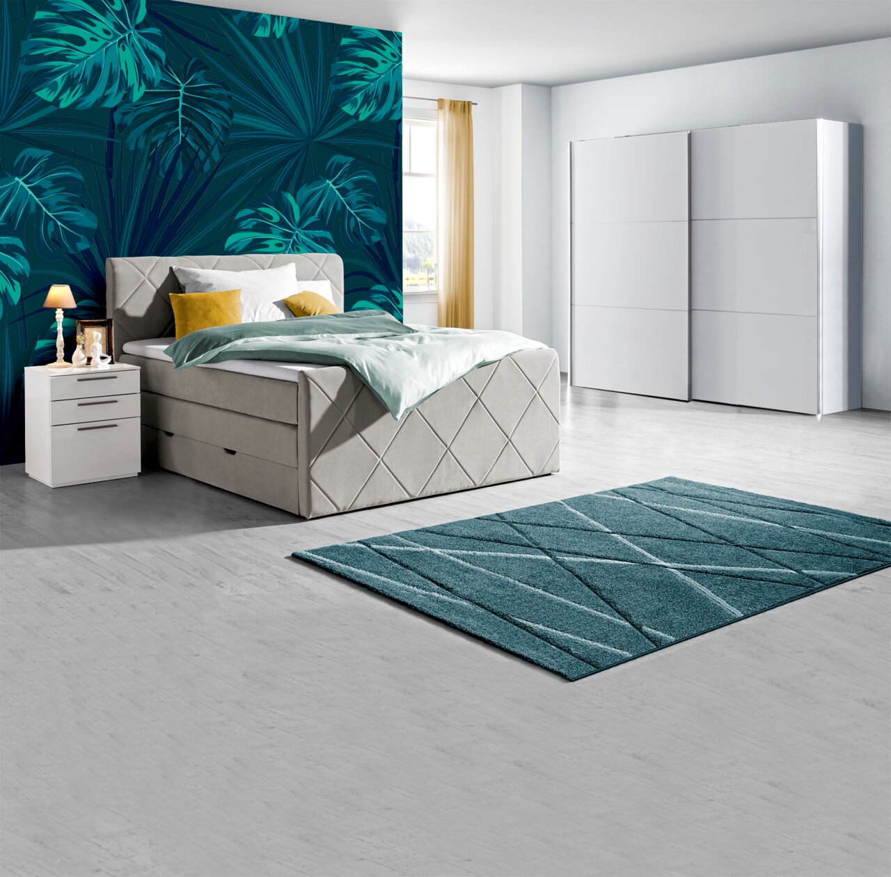 Modernes Schlafzimmer mit Boxspringbett in hellem Stoff, zwei weißen Nachttischen, einem großen weißen Schwebetürenschrank und einem türkisfarbenen Teppich, seitliche Perspektive.