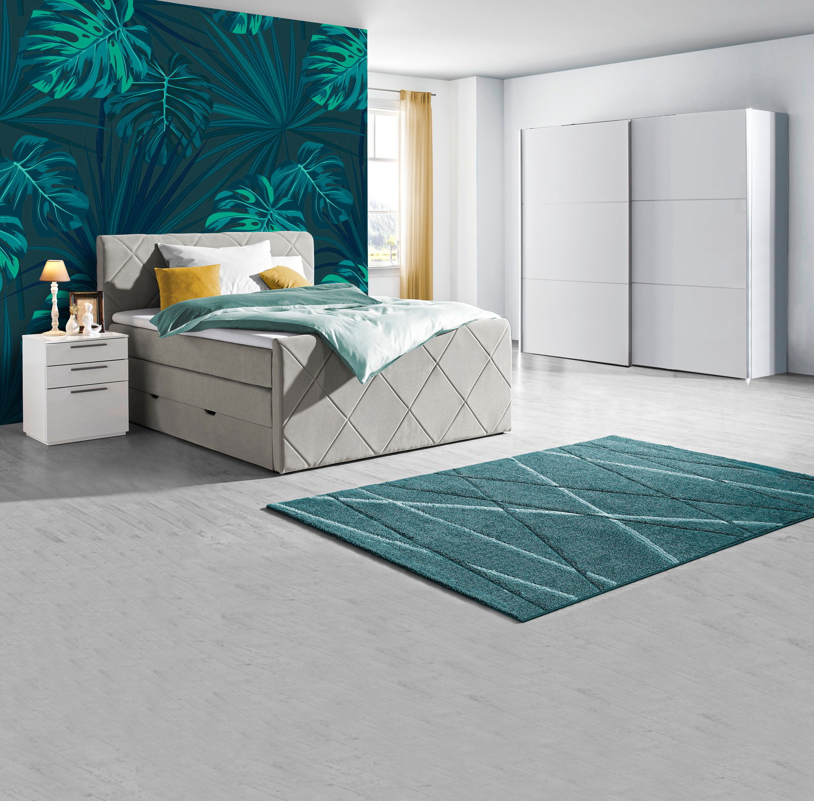 Modernes Schlafzimmer mit Boxspringbett in hellem Stoff, zwei weißen Nachttischen, einem großen weißen Schwebetürenschrank und einem türkisfarbenen Teppich, seitliche Perspektive.