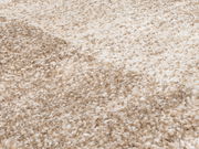 Nahaufnahme eines beigen, flauschigen Teppichs mit melierter Struktur, perspektivisch von der Seite aufgenommen.