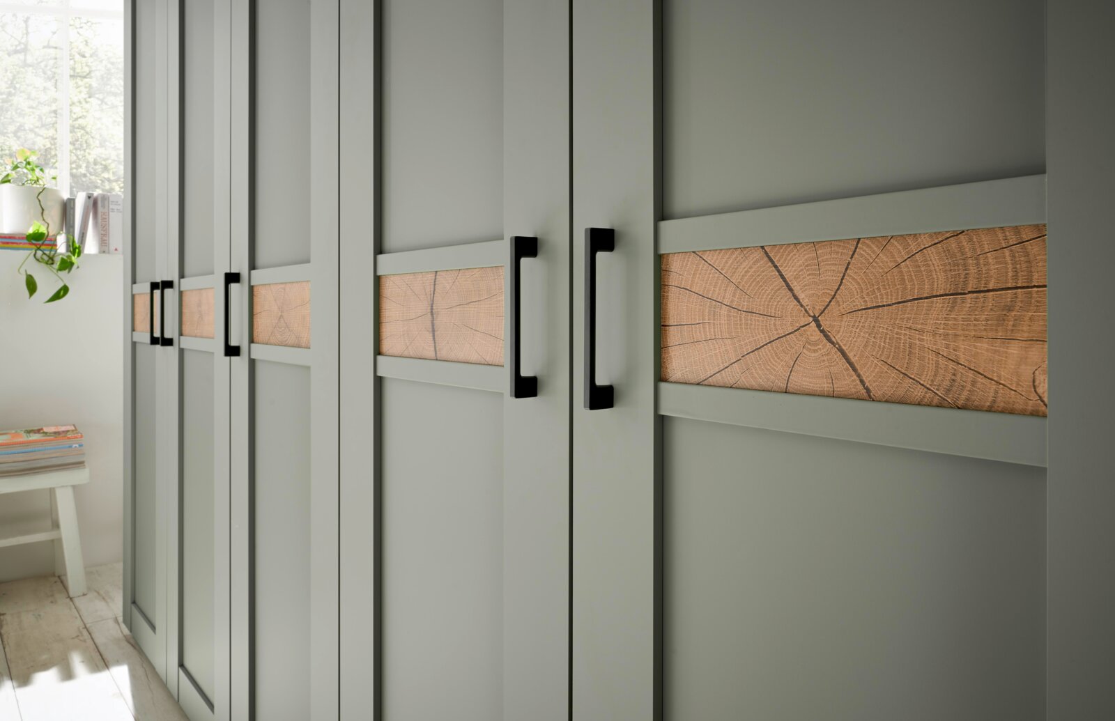 Schrankfront in Salbeigrün mit horizontalen Holzeinlagen und schwarzen Griffen, perspektivische Seitenansicht im hellen Raum