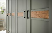 Schrankfront in Salbeigrün mit horizontalen Holzeinlagen und schwarzen Griffen, perspektivische Seitenansicht im hellen Raum