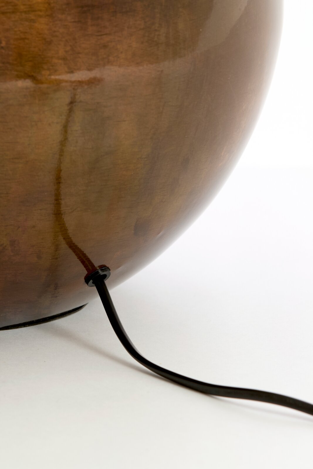 Close-up vanuit zijaanzicht van een afgeronde bruine lampvoet met zwart elektriciteitssnoer