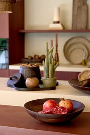 Donkerbruine decoratieve schaal met hele en opengesneden granaatappels, schuin van voren gefotografeerd in een sfeervol interieur.