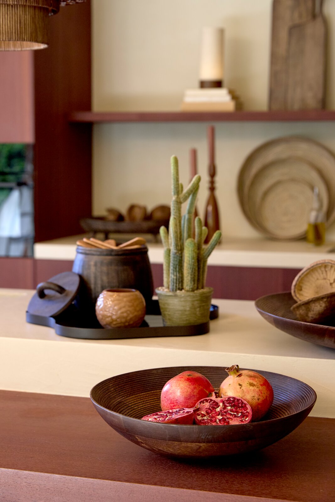 Donkerbruine decoratieve schaal met hele en opengesneden granaatappels, schuin van voren gefotografeerd in een sfeervol interieur.