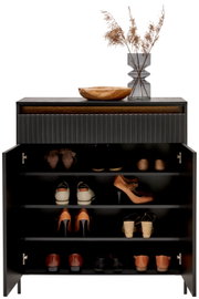 Moderne schoenenkast met open deur, gevuld met verschillende schoenen, versierd met een houten schaal en een vaas met gedroogde grassen bovenop, vooraanzicht.