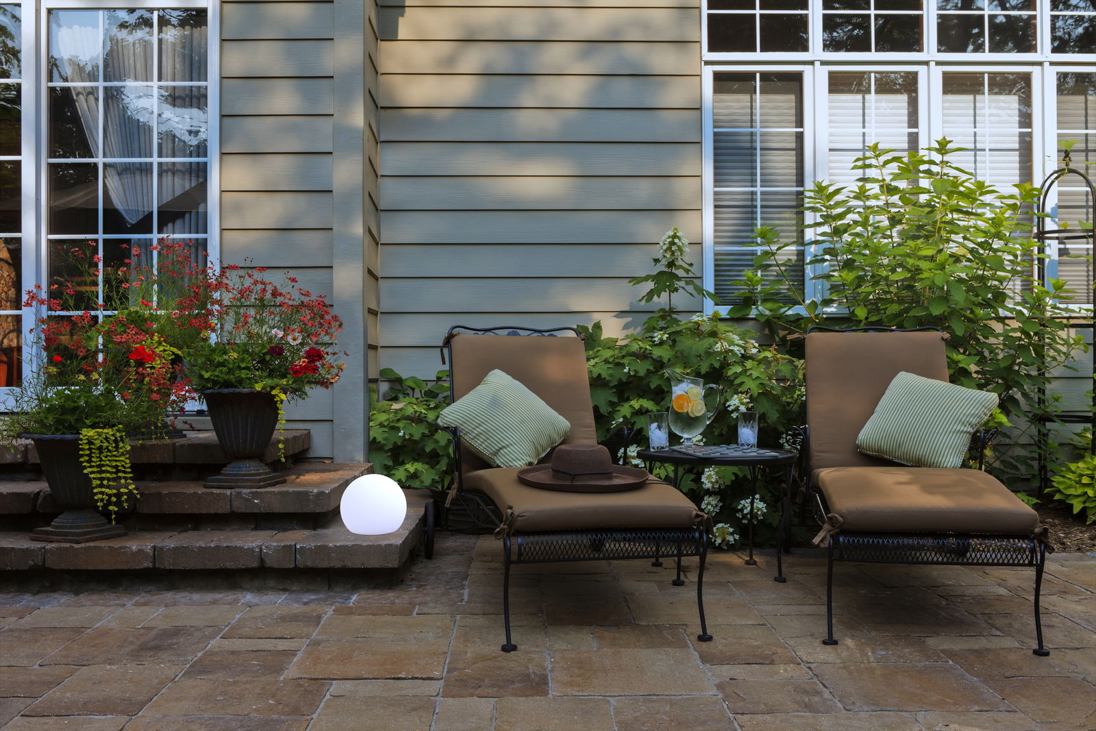 LED-Kugelleuchte Buly 20 kabel auf einer Terrasse, umgeben von Pflanzen und Gartenmöbeln, seitliche Perspektive
