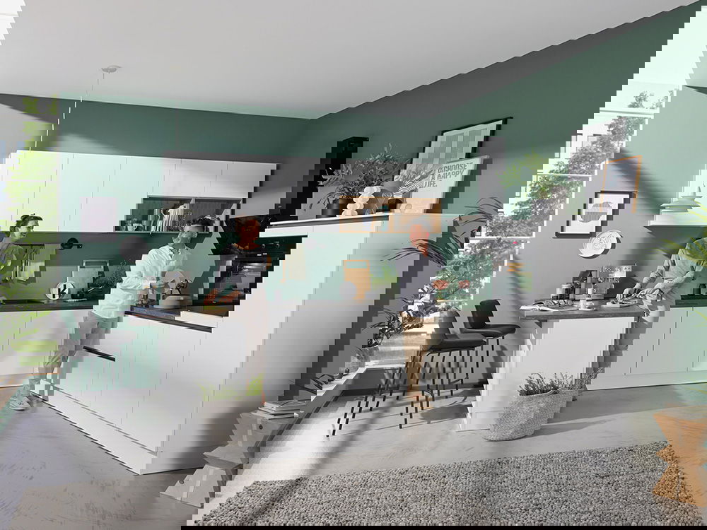 Moderne Küche in Weiß mit grüner Akzentwand, schwarzer Arbeitsplatte und wohnlicher Atmosphäre mit Pflanzen und Dekoration.