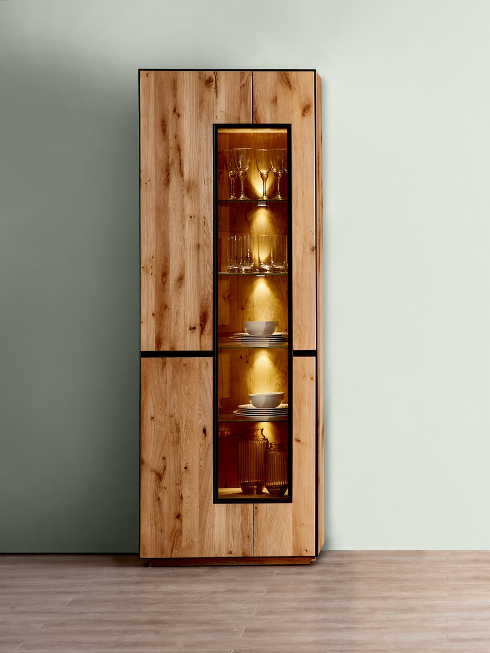 Linea Natura Vitrine mit Beleuchtung KELIO Vitrine mit Beleuchtung aus Holz, frontal fotografiert, mit Glastüren und beleuchteten Regalen, die Geschirr und Gläser präsentieren.