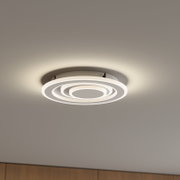 Moderne runde LED-Deckenleuchte in Weiß mit konzentrischen Leuchtringen, warmweiß leuchtend, an der Zimmerdecke montiert, Aufnahme aus leicht schräger Untersicht