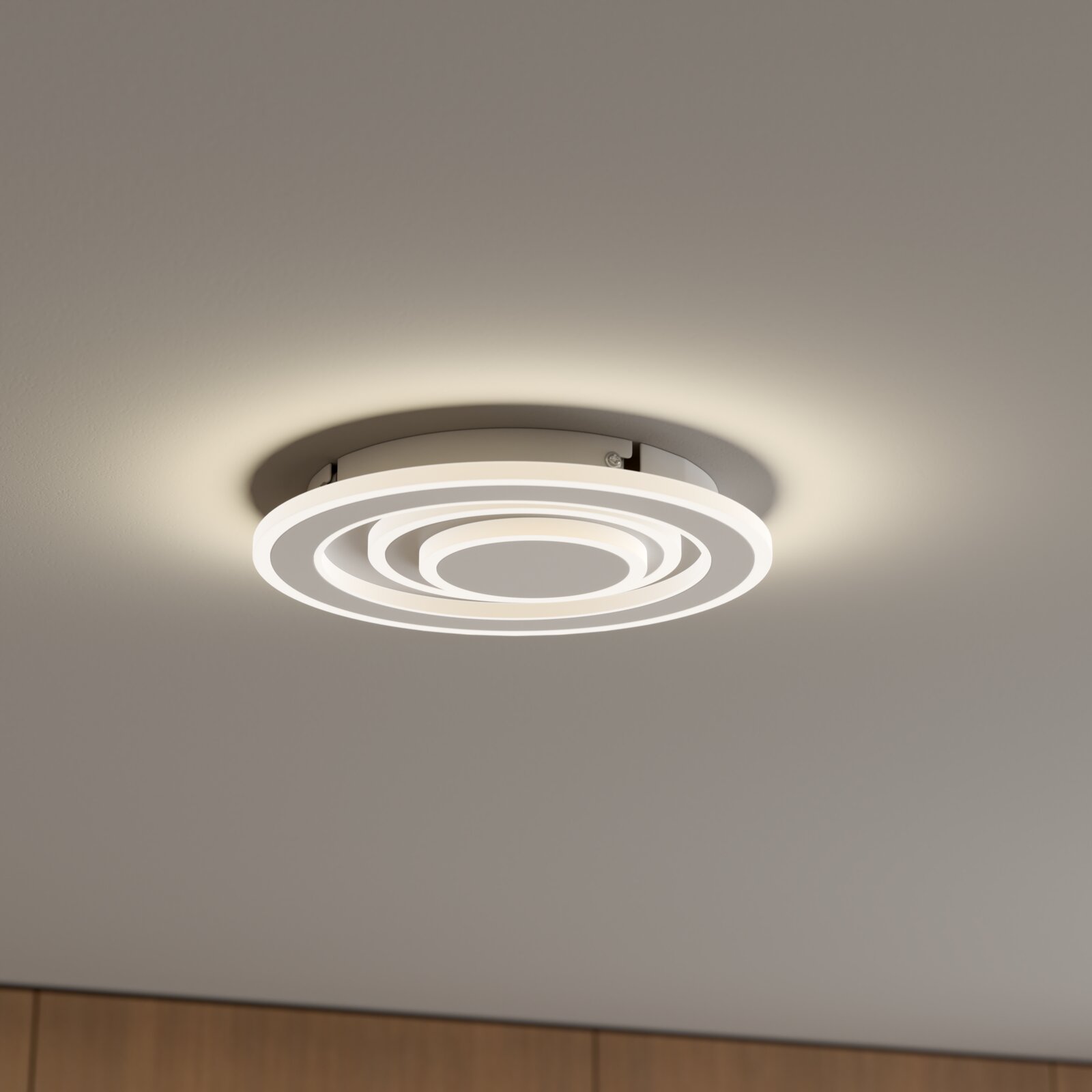 Moderne runde LED-Deckenleuchte in Weiß mit konzentrischen Leuchtringen, warmweiß leuchtend, an der Zimmerdecke montiert, Aufnahme aus leicht schräger Untersicht