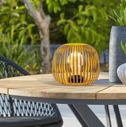 Gelbe Solarleuchte in moderner Gitteroptik auf einem Holztisch im Freien, seitliche Perspektive