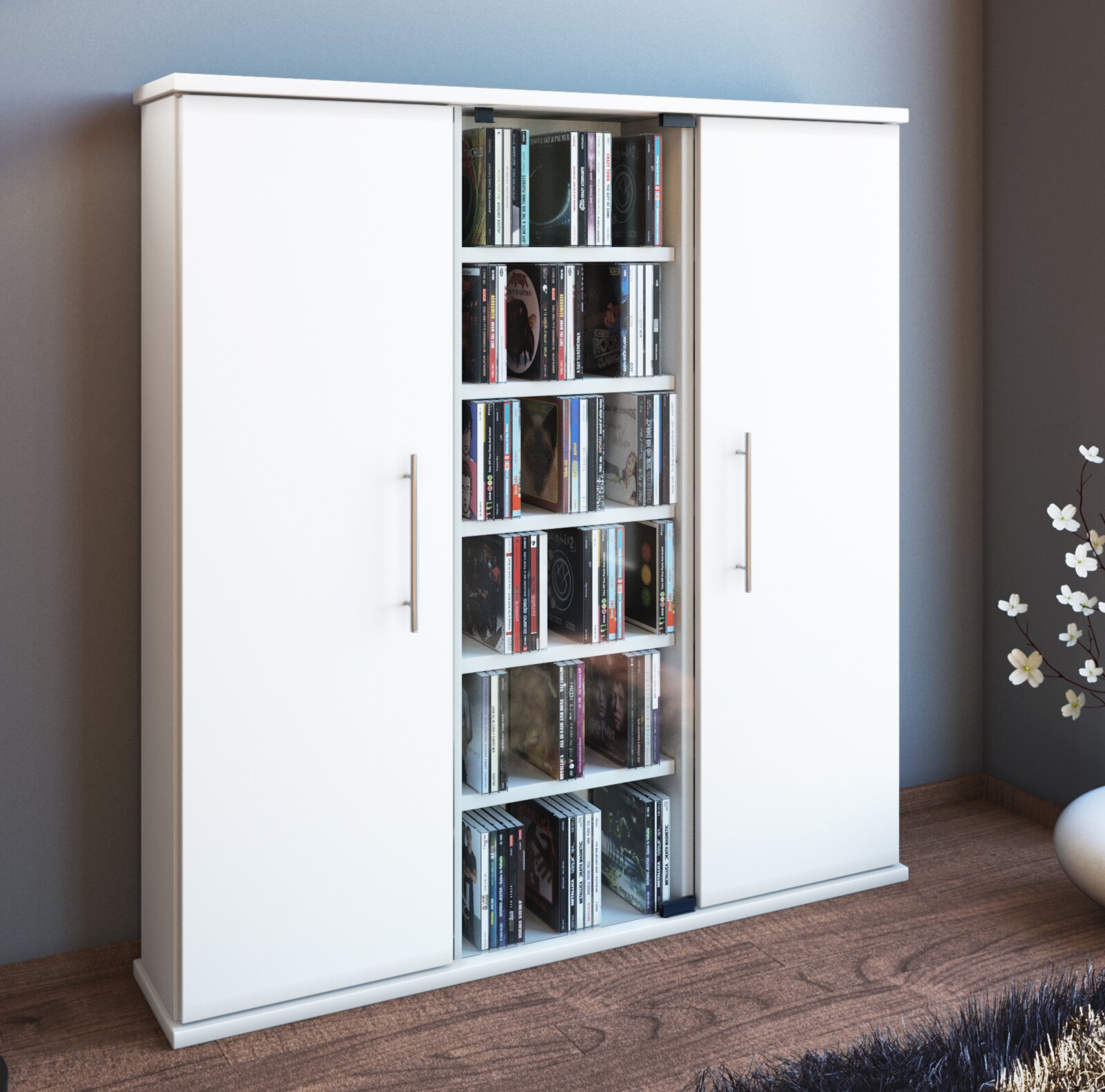 Weißer Schrank mit zwei Türen und offenem Mittelregal voller CDs, moderne Metallgriffe, in Wohnraum auf Holzboden – Frontansicht in leichter Schrägperspektive von links.