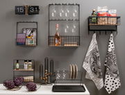 Wanduhr im Flip-Design von KARLSSON, schwarz, ohne Gehäuse, an einer grauen Wand montiert, umgeben von modernen Küchenregalen und Dekorationen.