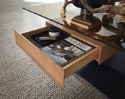 Moderner Couchtisch mit Glasplatte und offener Schublade, gefüllt mit Zeitschriften und Dekoration, aus der Perspektive von oben.