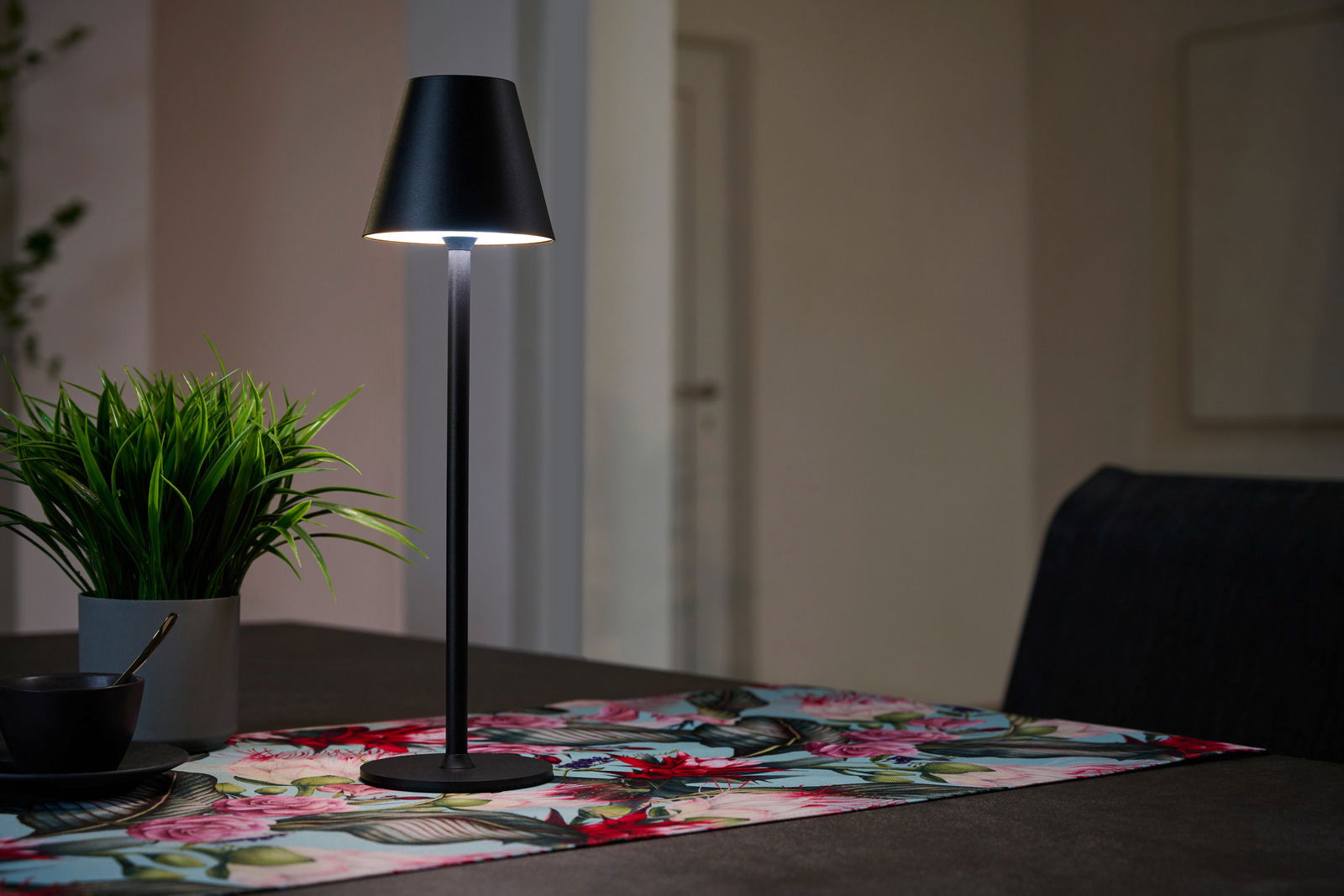 Schwarze Akku-Tischleuchte auf einem Tisch mit bunter Tischdecke, seitliche Perspektive