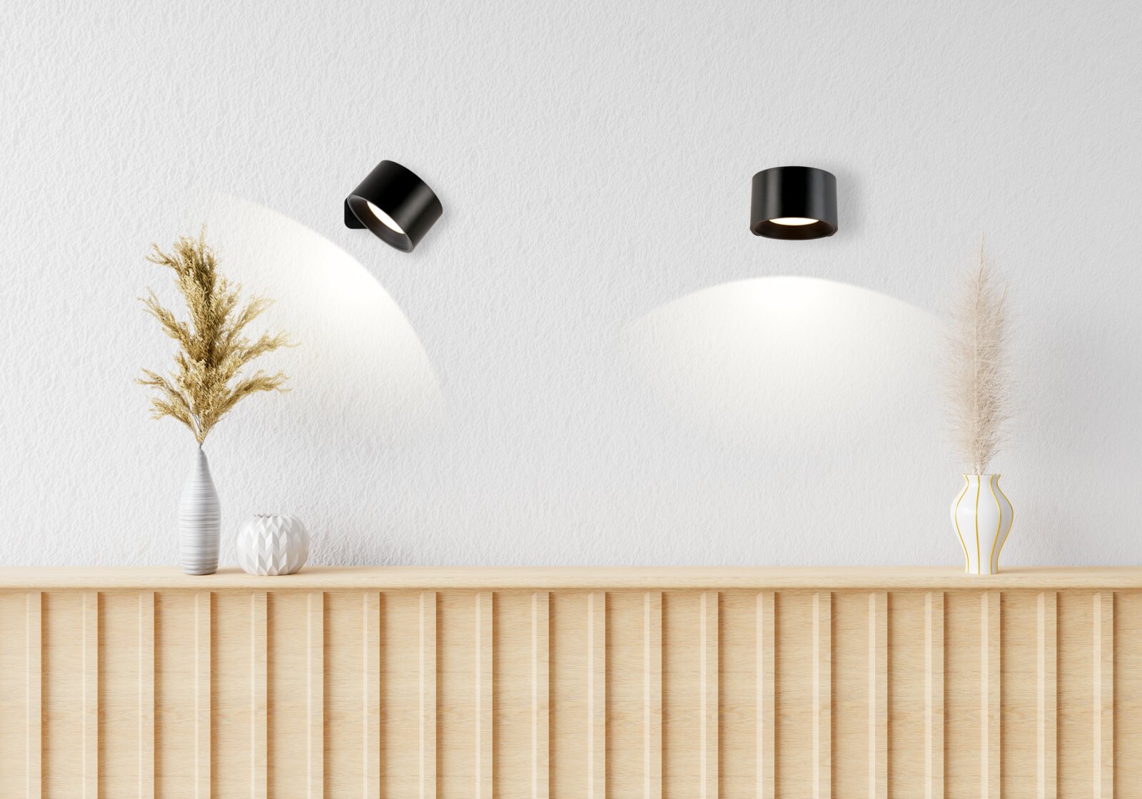 Zwei schwarze Decken-Aufbaustrahler in einem minimalistischen Raum, einer schwenkbar, mit warmem Lichtkegel an der weißen Wand; Perspektive: frontale Ansicht mit leichtem Blick nach oben.