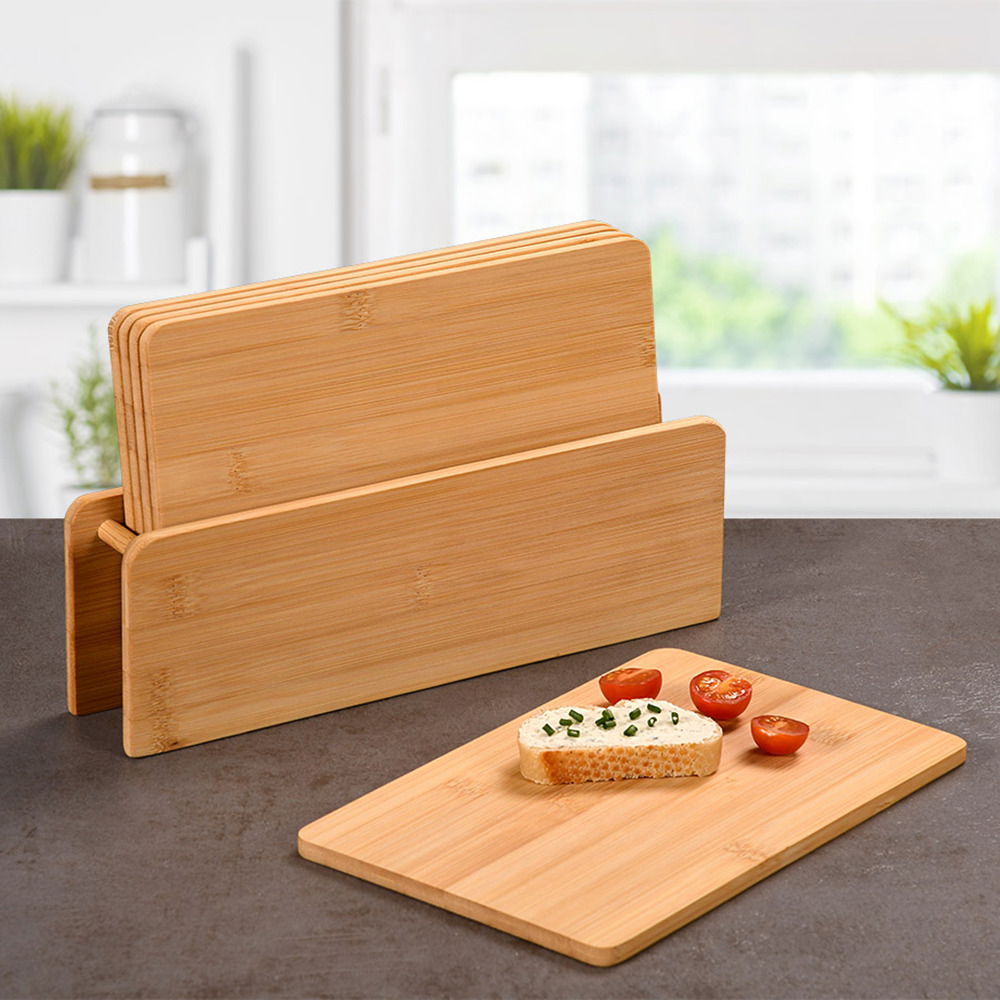 Kesper Brettchenständer inkl. 5 Brettchen Brettchenständer mit fünf Bambus-Brettchen, eines davon mit Brot und Tomaten belegt, auf einer Küchenarbeitsplatte vor einem Fenster, seitliche Perspektive.