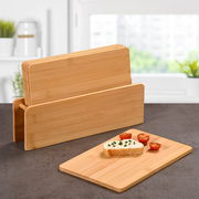 Brettchenständer mit fünf Bambus-Brettchen, eines davon mit Brot und Tomaten belegt, auf einer Küchenarbeitsplatte vor einem Fenster, seitliche Perspektive.