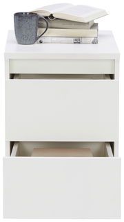 Weiße Nachtkommode mit zwei offenen Schubladen, darauf Bücher und eine Tasse, Frontalansicht