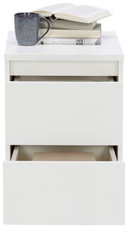 Weiße Nachtkommode mit zwei offenen Schubladen, darauf Bücher und eine Tasse, Frontalansicht