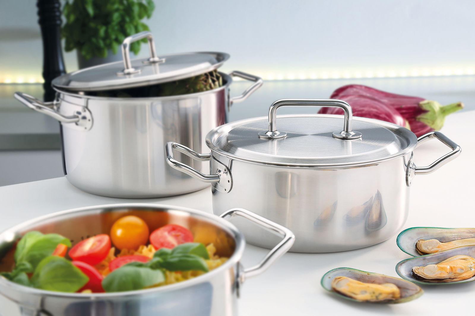 Topfset Brigade Premium 4-tlg. aus Edelstahl, in einer modernen Küche präsentiert, mit frischen Zutaten und Muscheln im Vordergrund, seitliche Perspektive