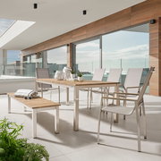 Moderne Outdoor-Essgruppe auf einer Terrasse: rechteckiger Tisch mit Holzplatte und Metallgestell, dazu helle Stühle und passende Bank, seitliche Frontansicht in leichter Perspektive